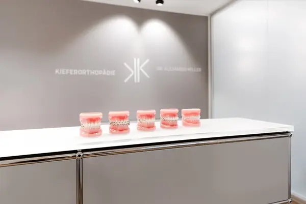 Fünf Zahnspangen-Modelle stehen auf einem Tresen in moderner Kieferorthopädie Praxis.