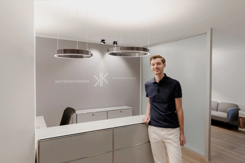 Moderner Empfangsbereich einer Kieferorthopädie Praxis mit freundlichem Mitarbeiter.